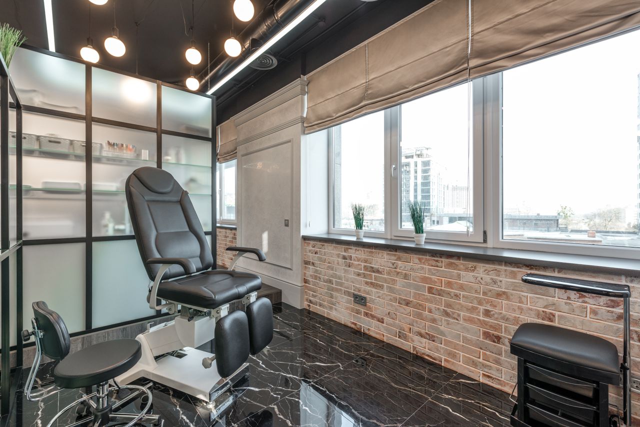 Black leather pedicure chair placed near brick wall in modern beauty salon with window and stylish interior with glowing lamps